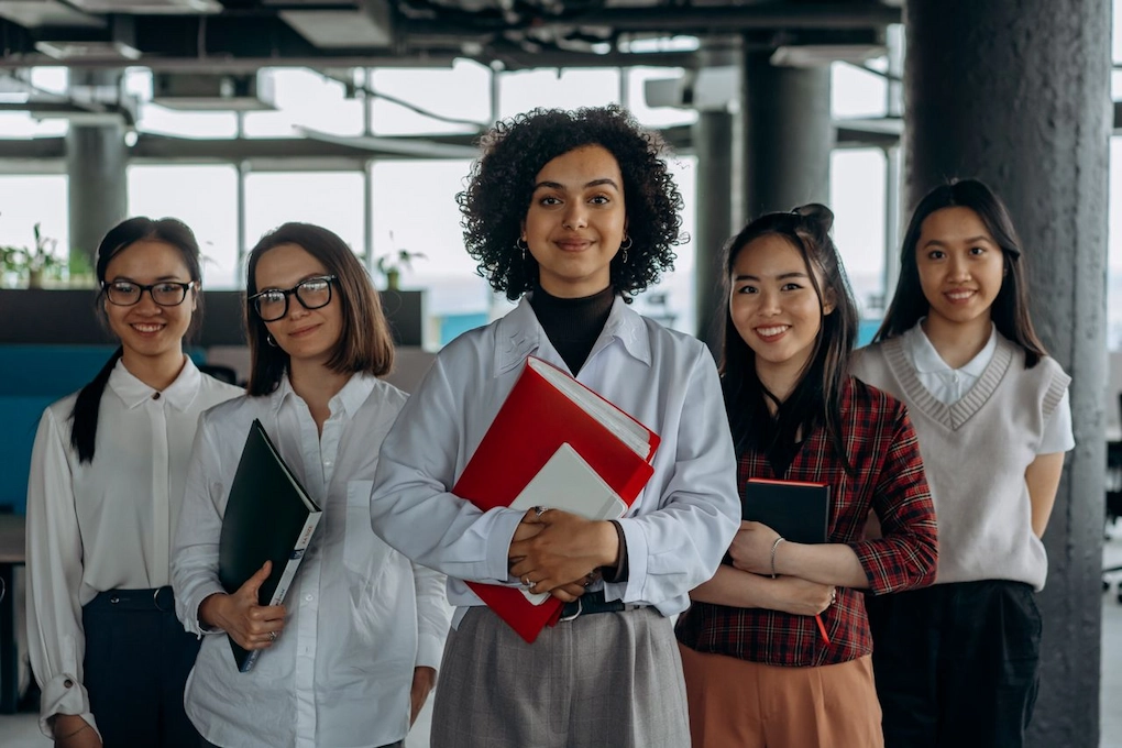 Women colleagues standing in a modern office setting, holding documents. What to Do If You Keep Getting Rejected for Business Grants
