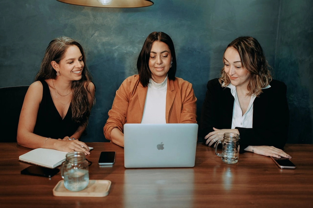 Three women talking business in a modern office. Business grants for women in Alaska.