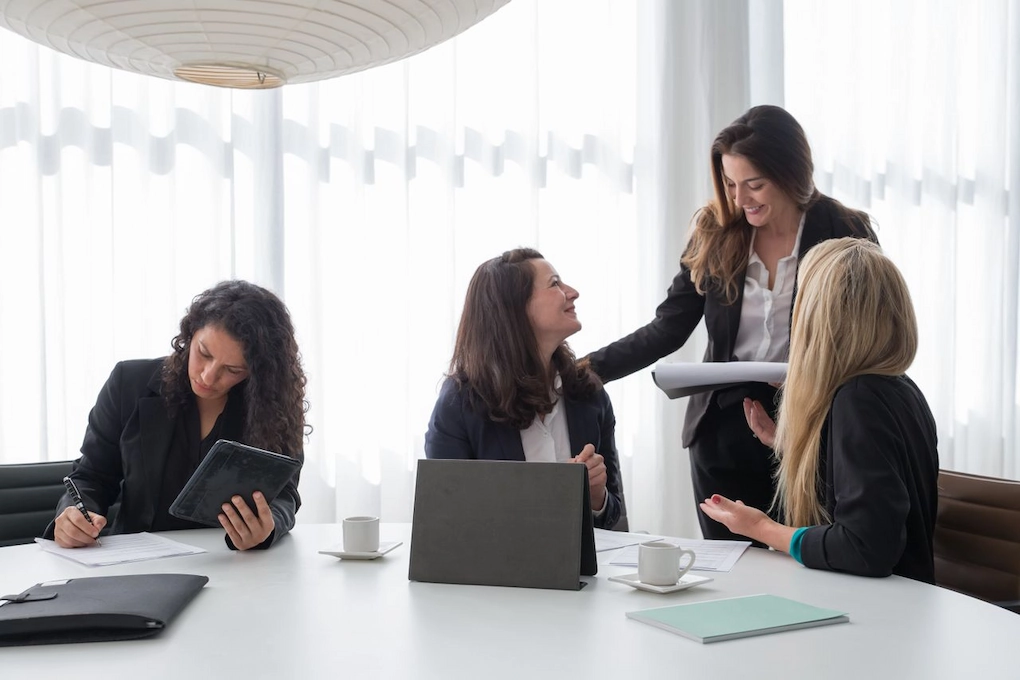 Four women in professional attire working together in an office. Business grants for women in Connecticut