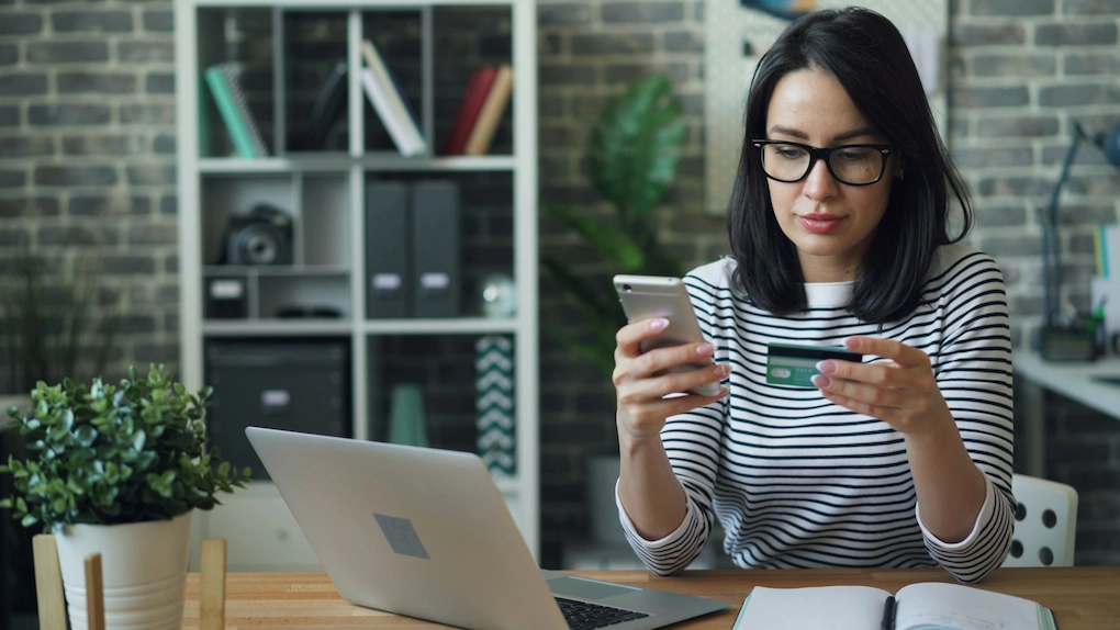 A woman making a payment with a credit card using a smartphone. Business grant scams