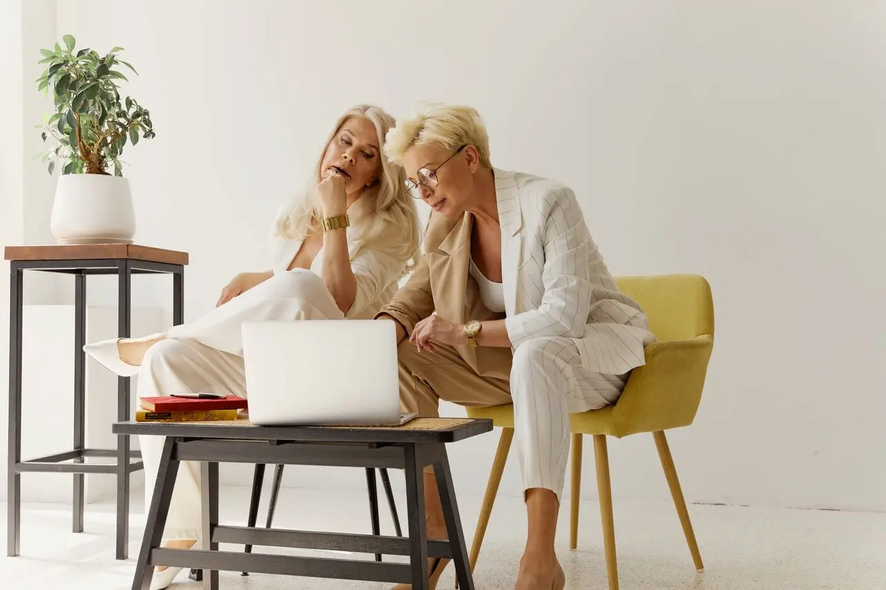 Two women discussing business over a laptop in a modern office setting