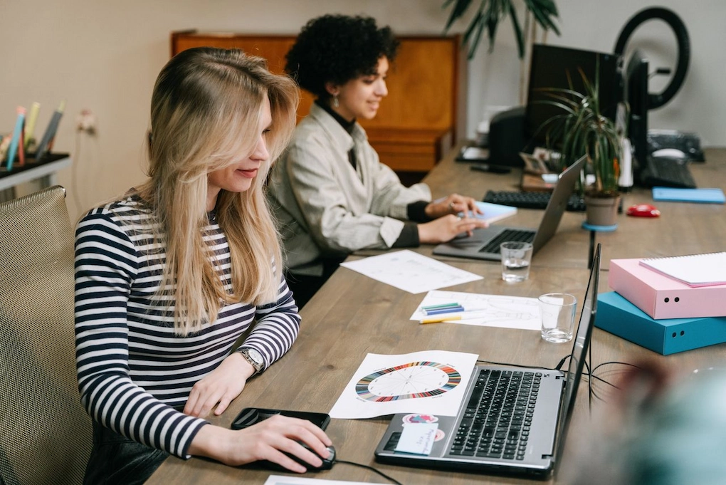 Two women collaborating at their laptops in a modern office setting. Business Grants for Women in Iowa